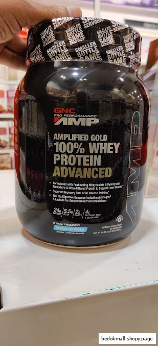 Hand holding a GNC Amplified Gold 100% Whey Protein Advanced container.