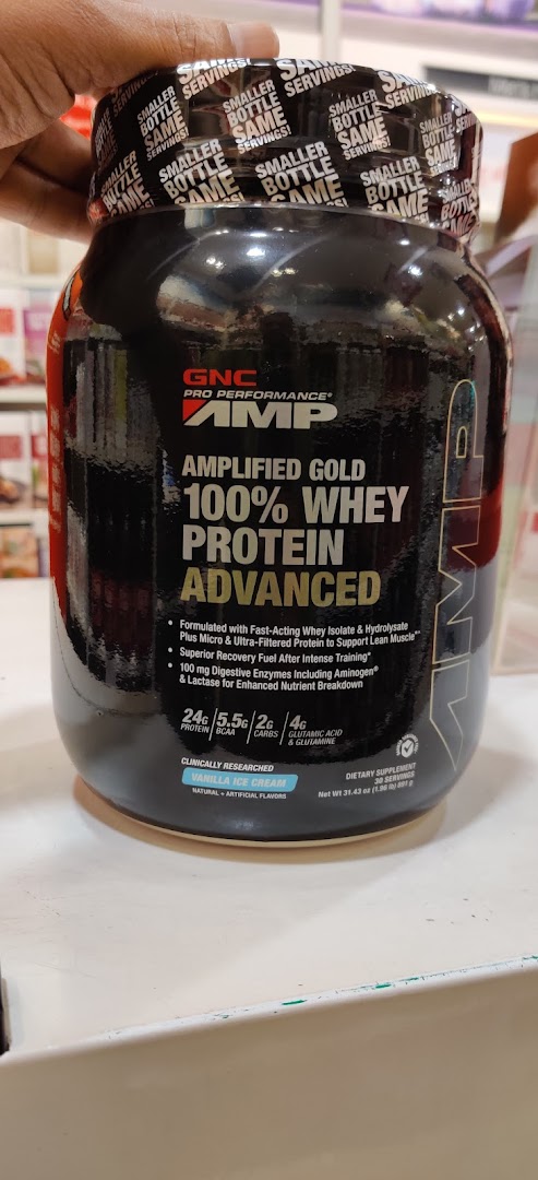 Hand holding a large black container of GNC whey protein.