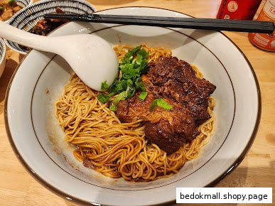 A bowl of noodles with braised meat, green onions, and a spoon.
