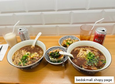 Two bowls of noodles, side dishes, and drinks on a wooden table.