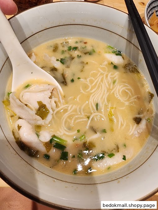 Close-up of a bowl of fish noodle soup with a spoon and chopsticks.