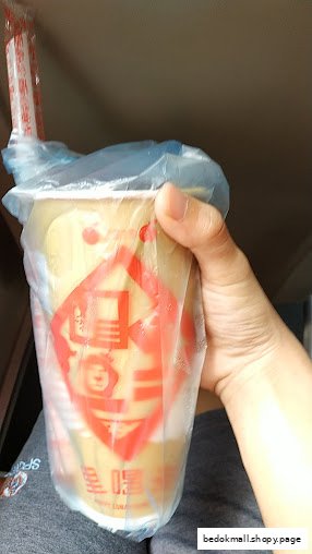 A hand holds a large drink in a plastic bag with a straw.