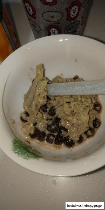 A bowl of creamy dessert with dark pearls and a straw.