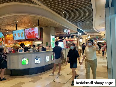 Bubble tea counter with staff and customers in a mall setting.