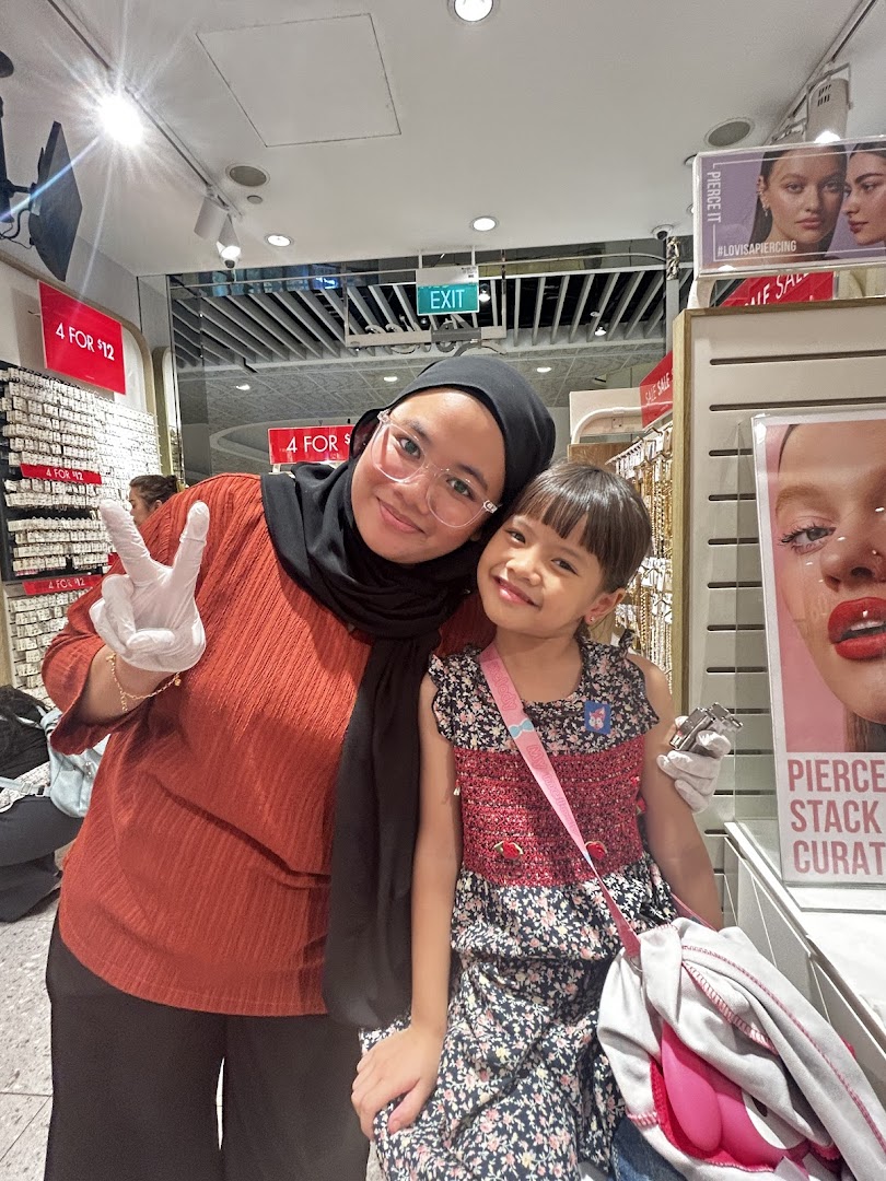 Two people posing inside a Lovisa store with merchandise displays and promotional signs.