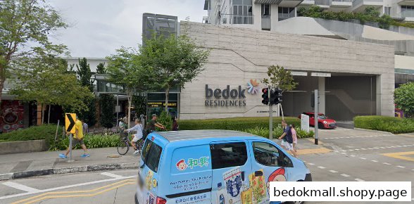 Exterior view of a large building complex with people, trees, and a street.