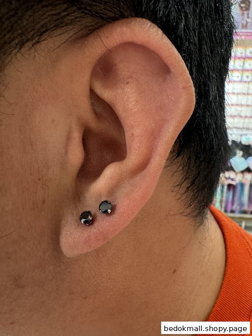 Close-up of an ear with two black stud earrings.
