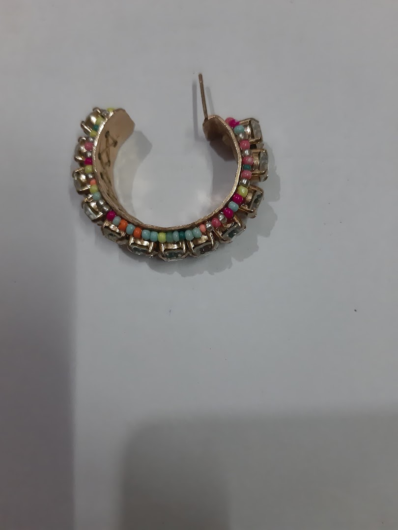 Close-up of a single gold hoop earring with colorful beads and clear stones.