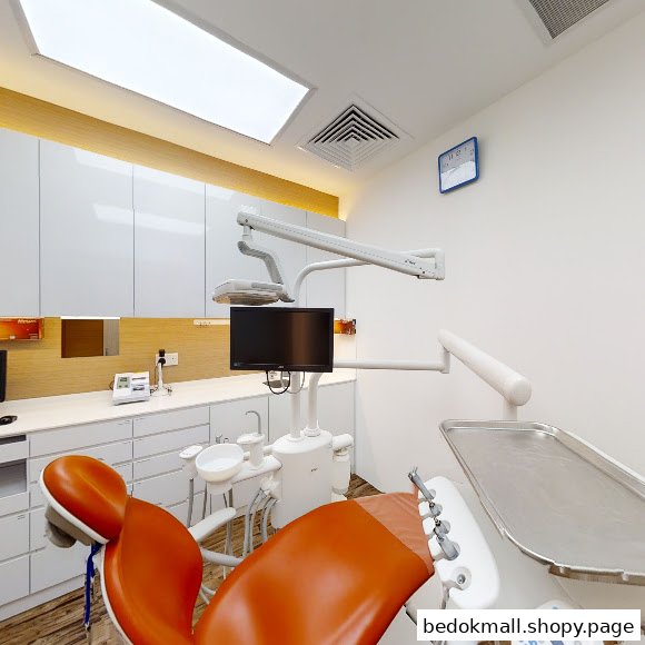 Interior view of a dental clinic room with an orange dental chair and equipment.