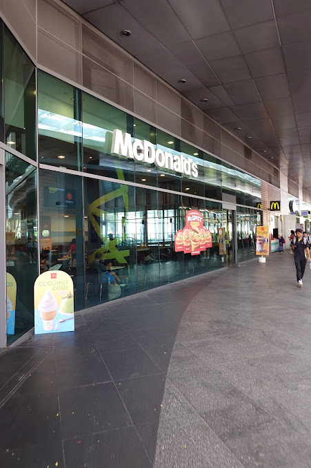Exterior view of a McDonald's restaurant with a glass facade and people walking by.