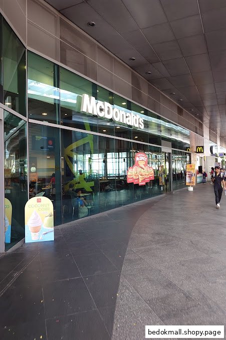 Exterior view of a McDonald's restaurant with a glass facade and people walking by.