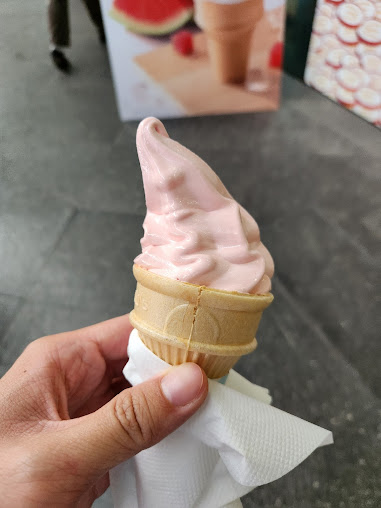 A hand holds a pink soft-serve ice cream cone.