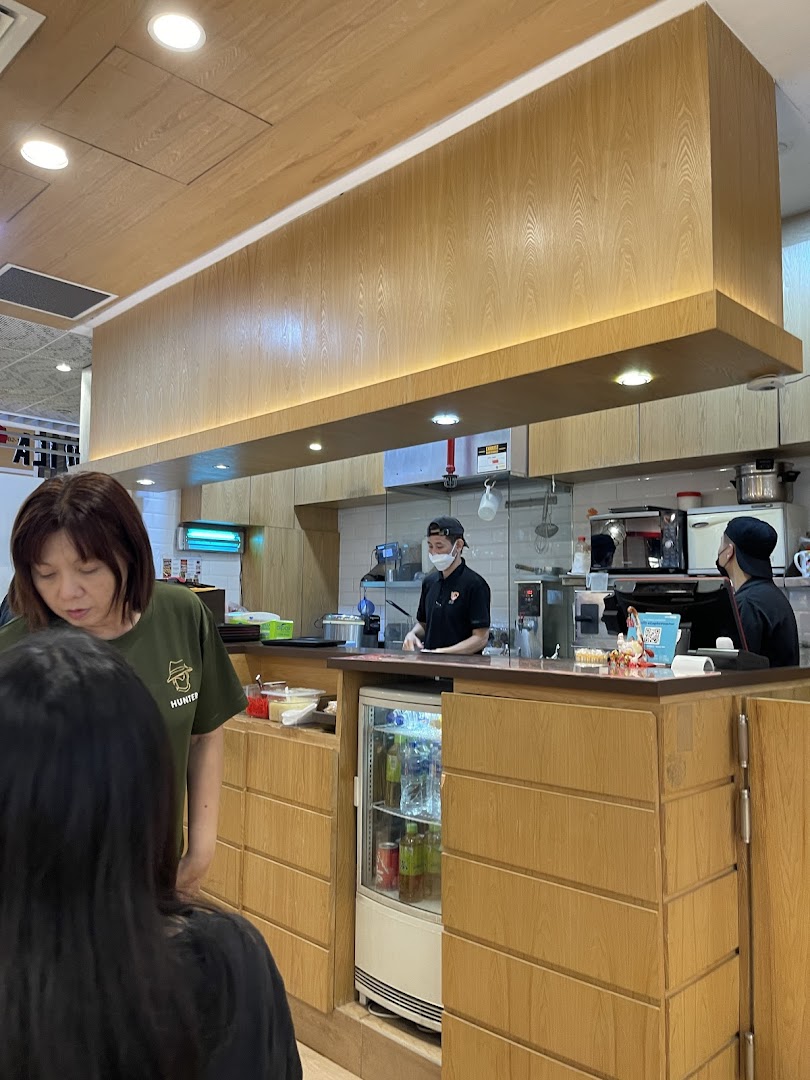 Customers and staff at a food counter with an open kitchen area.