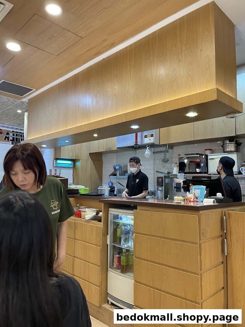 Customers and staff at a food counter with an open kitchen area.