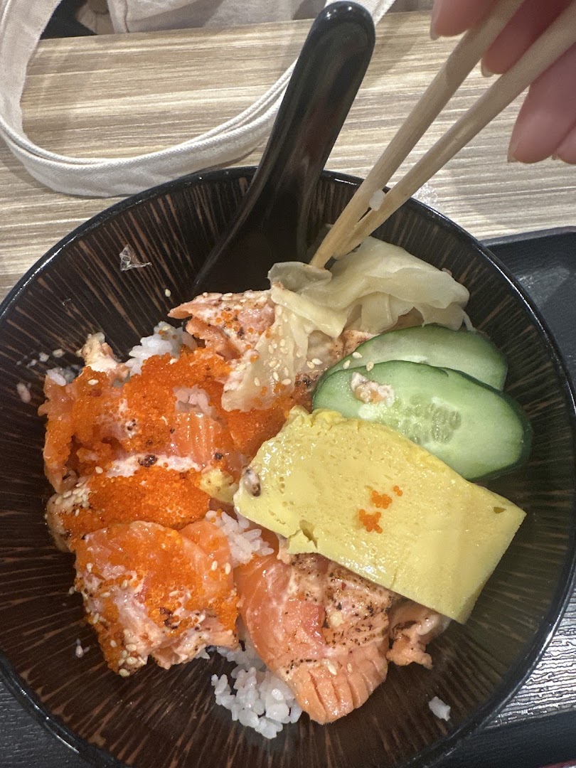 A salmon donburi with egg, cucumber, and roe, being eaten with chopsticks.