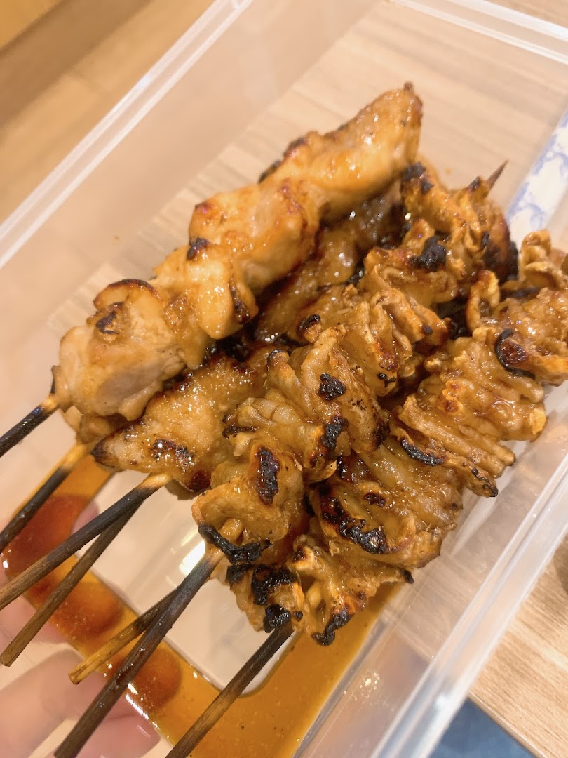 Close-up of grilled meat skewers with sauce in a plastic container.