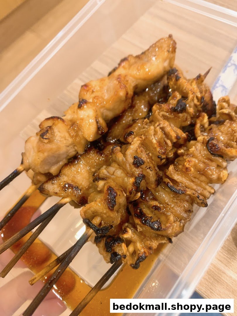Close-up of grilled meat skewers with sauce in a plastic container.