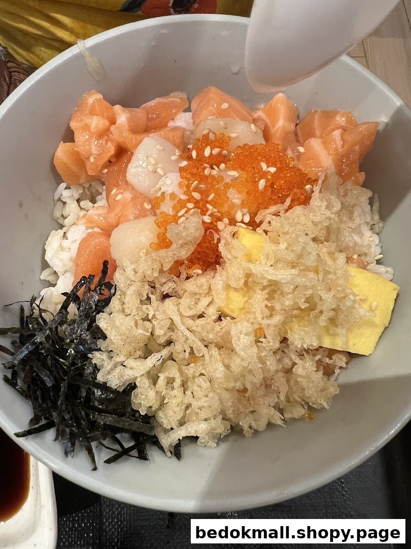 A bowl of rice with salmon, scallops, roe, tempura bits, and seaweed.