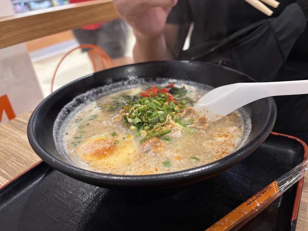 A person eating a bowl of ramen with chopsticks and a spoon.