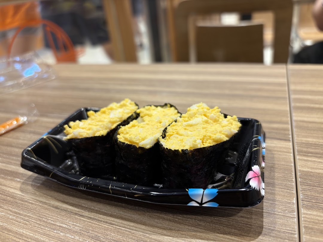 Three egg salad sushi pieces in a black tray on a wooden table.
