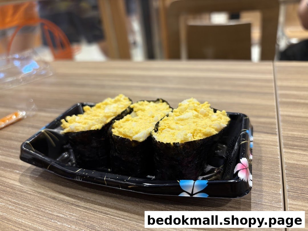 Three egg salad sushi pieces in a black tray on a wooden table.