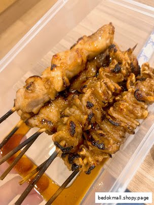 Grilled meat skewers in a clear plastic container with sauce.