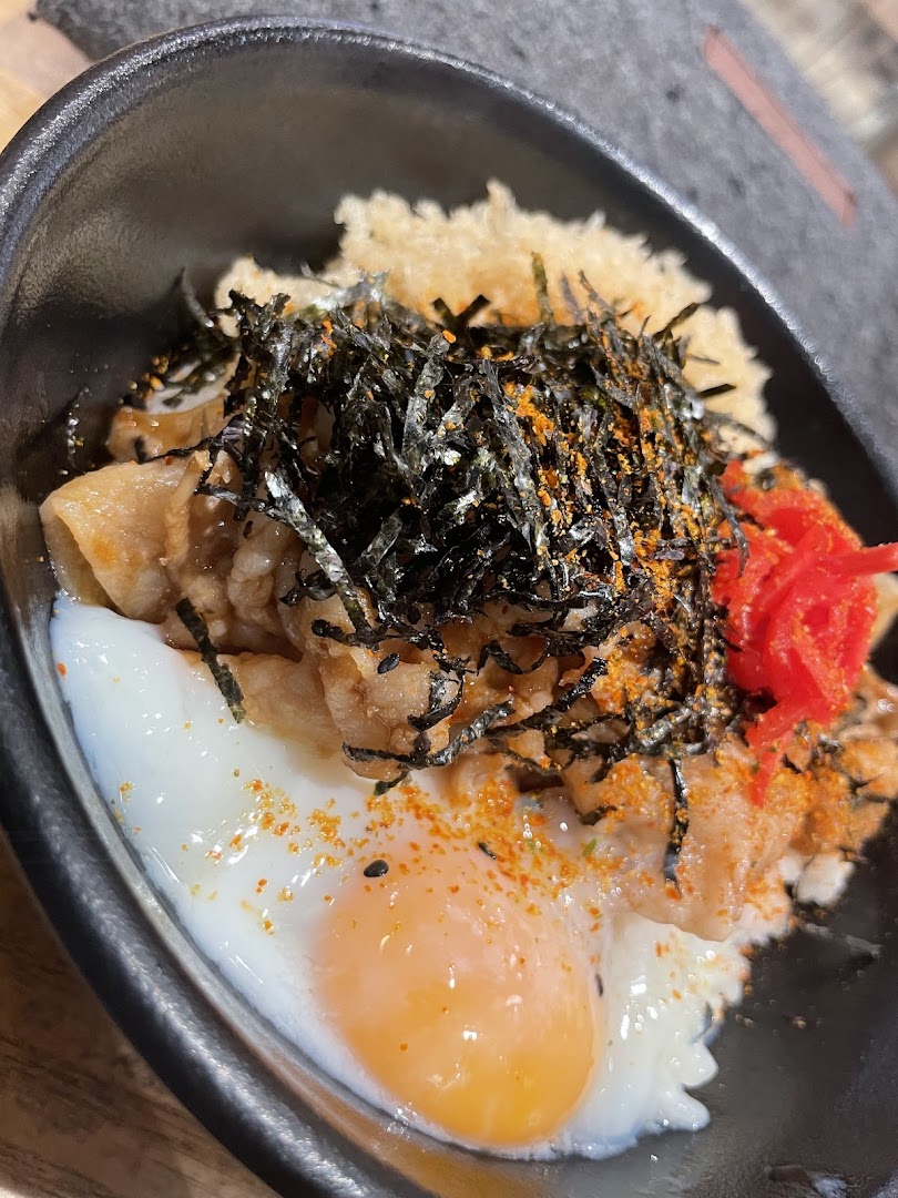 Close-up of a rice bowl with meat, egg, and seaweed in a black bowl.