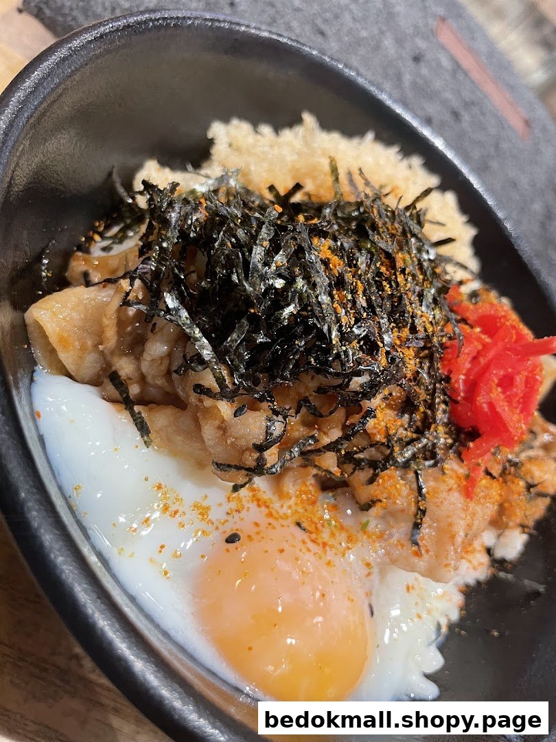 Close-up of a rice bowl with meat, egg, and seaweed in a black bowl.