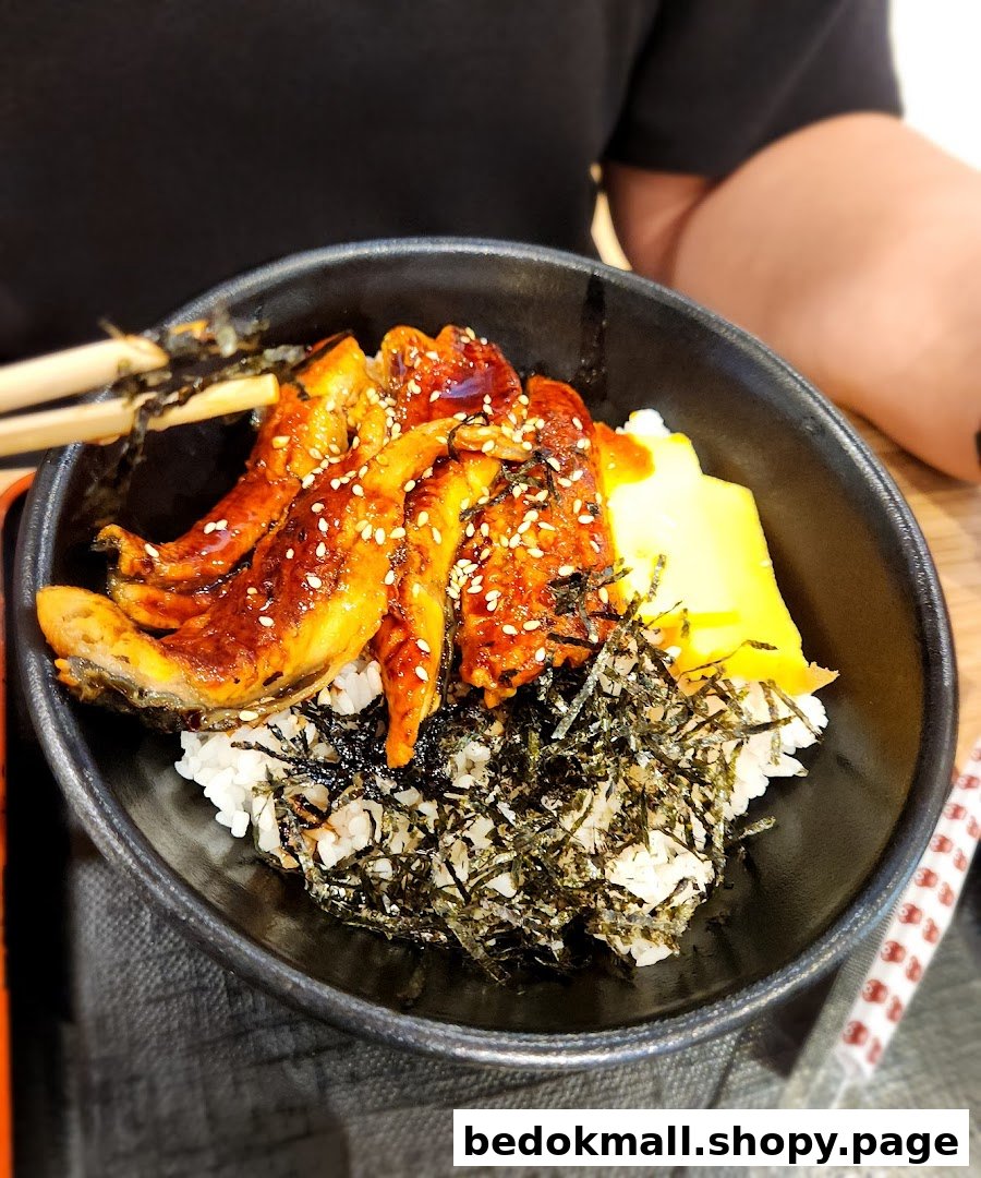 A close-up of a bowl of eel rice with seaweed and egg.