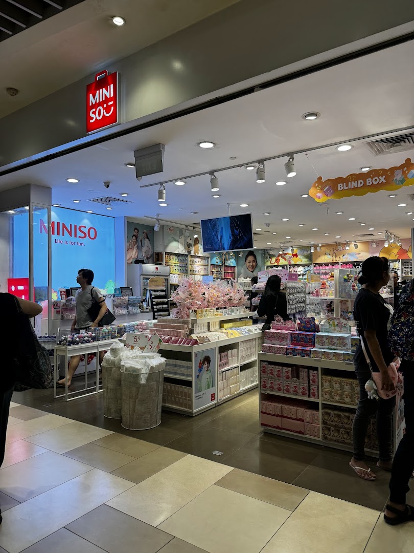 MINISO store entrance from the mall corridor, showing products and customers.