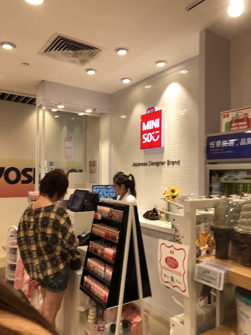 Customer at checkout counter inside a MINISO store with staff and products.