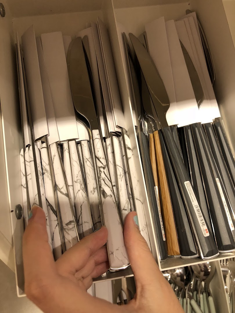 Hand holding a marble-handled knife among other cutlery in a display.