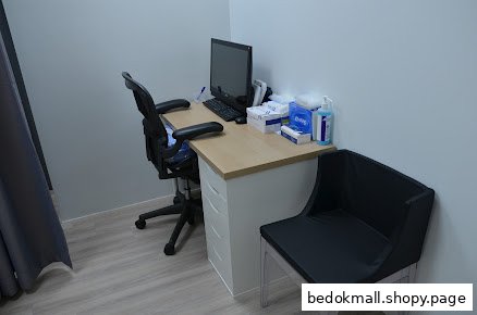 Clinic examination room with a desk, computer, office chair, and visitor chair.