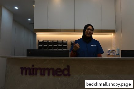 A staff member stands behind a reception desk with the Minmed logo.