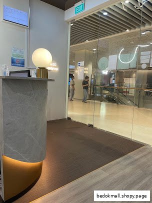 Interior view of a clinic reception desk and glass exit door leading to a mall.