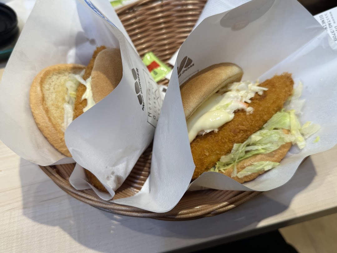 Two burgers in paper wrappers are served in a wicker basket.