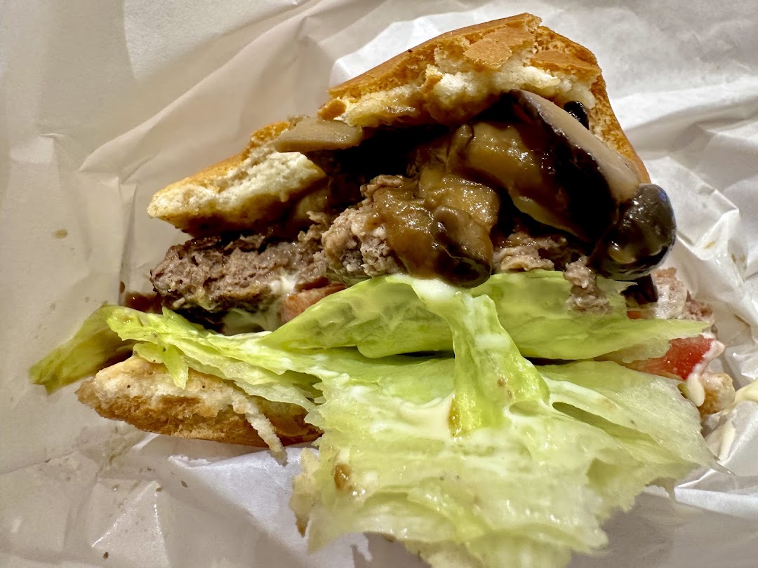Close-up of a burger with patty, mushrooms, lettuce, and tomato in wrapping.