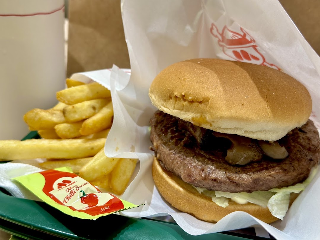 A burger with mushrooms, french fries, and a chili sauce packet.
