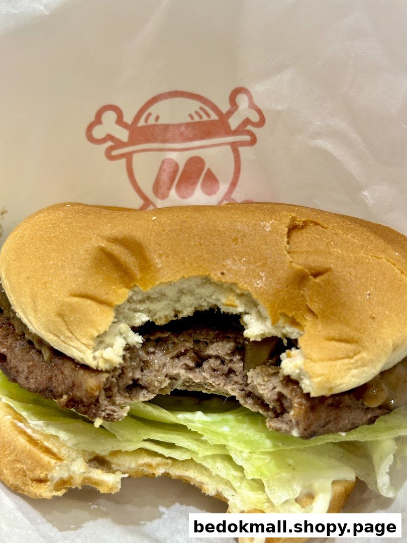 A partially eaten burger with lettuce and patty, on a wrapper with a logo.