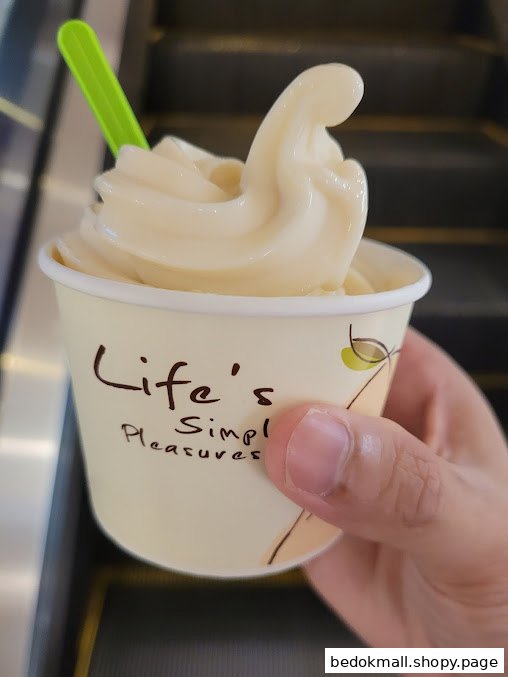 Close-up of a hand holding a soft-serve ice cream cup with a green spoon.