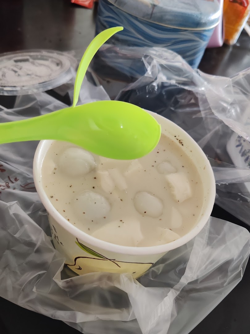 A cup of white dessert with small balls and cubes, and a green spoon.