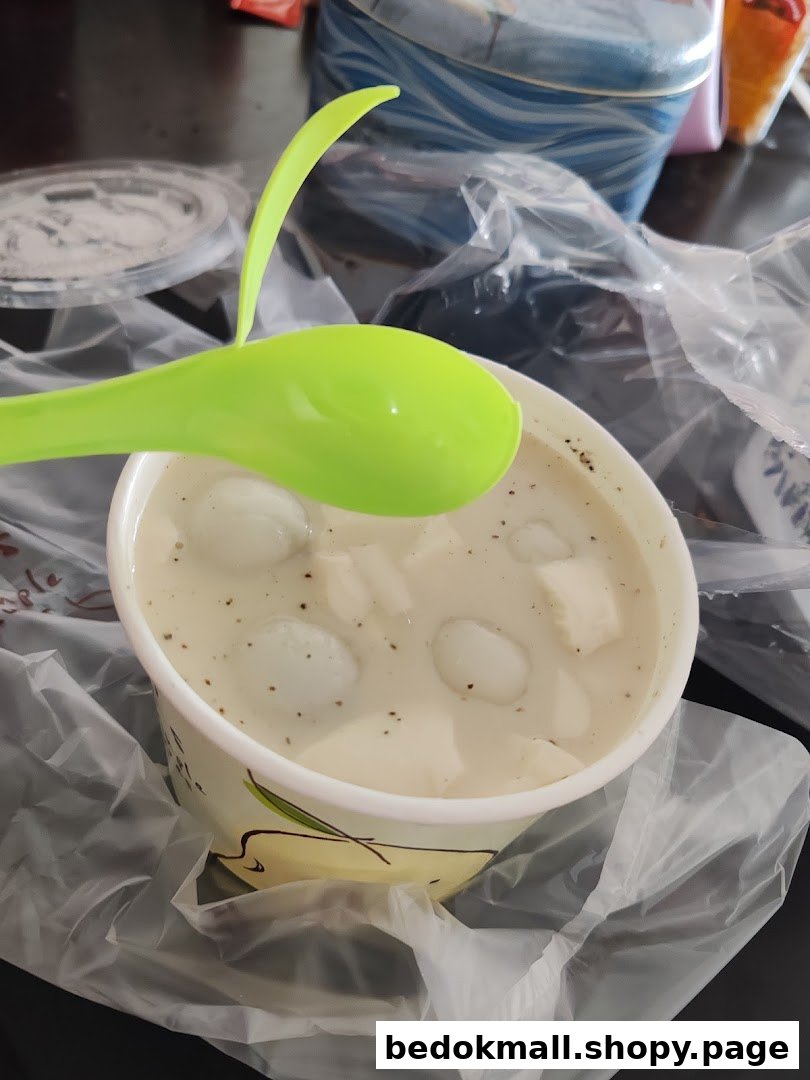 A cup of white dessert with small balls and cubes, and a green spoon.