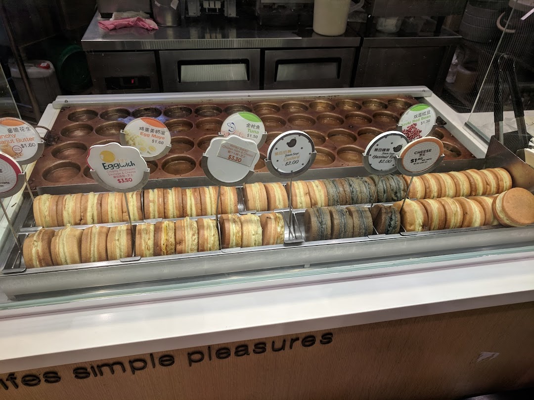 Display of freshly made round pastries with various fillings and price tags.