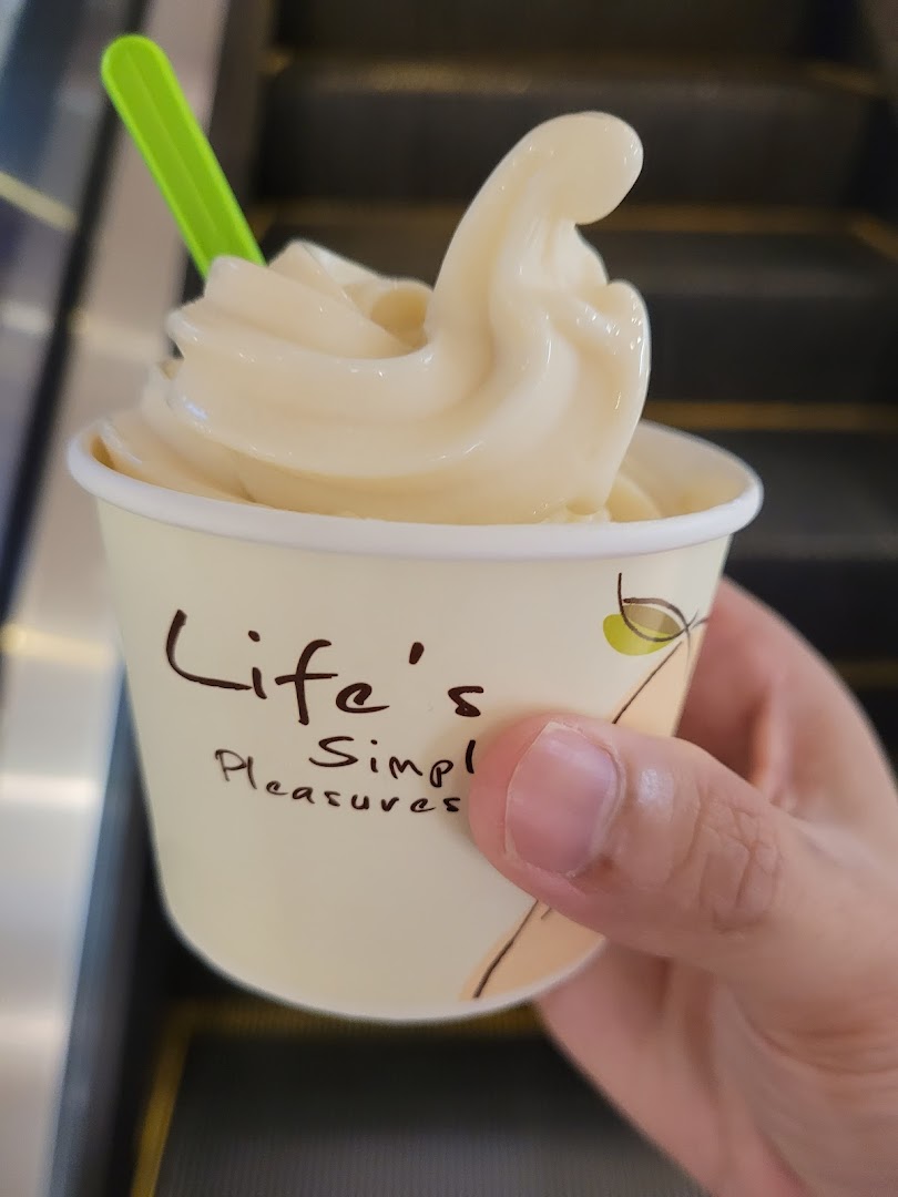 Hand holding a cup of soft-serve ice cream with a green spoon.
