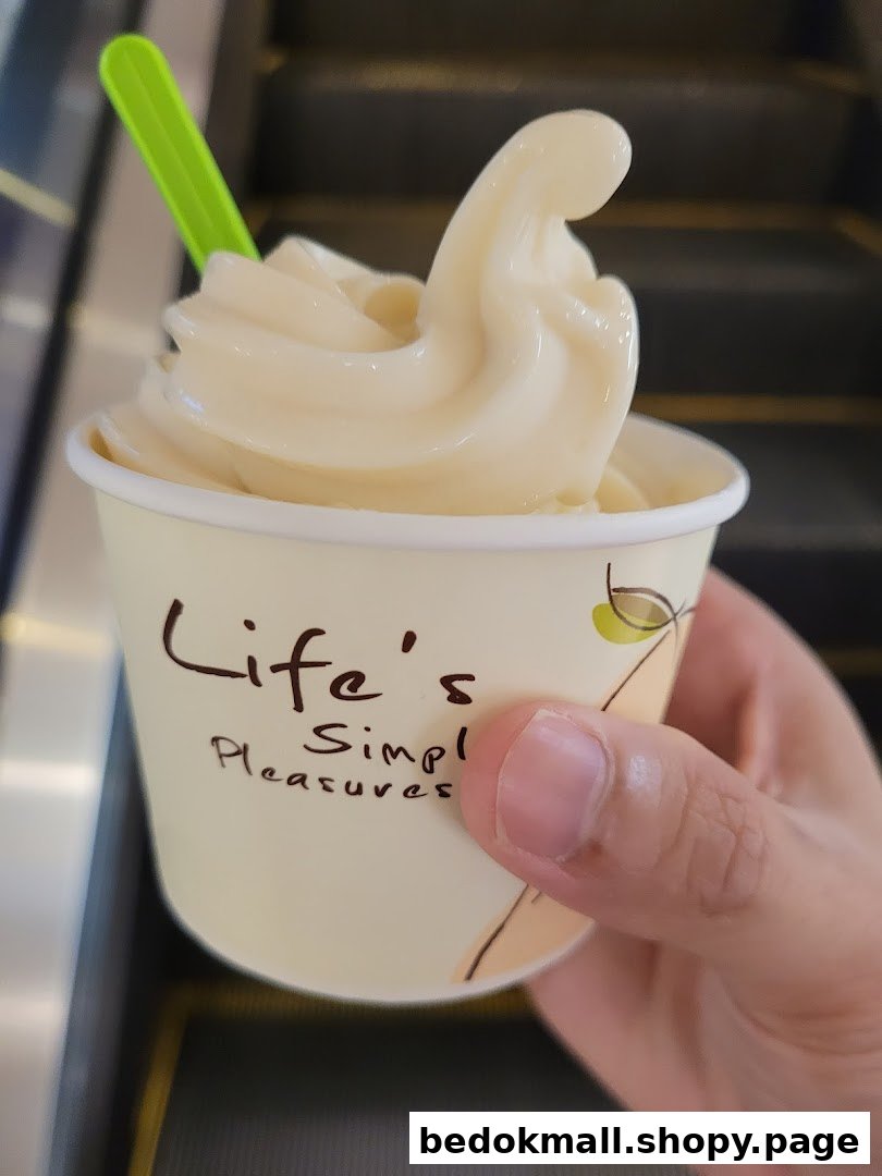 Hand holding a cup of soft-serve ice cream with a green spoon.
