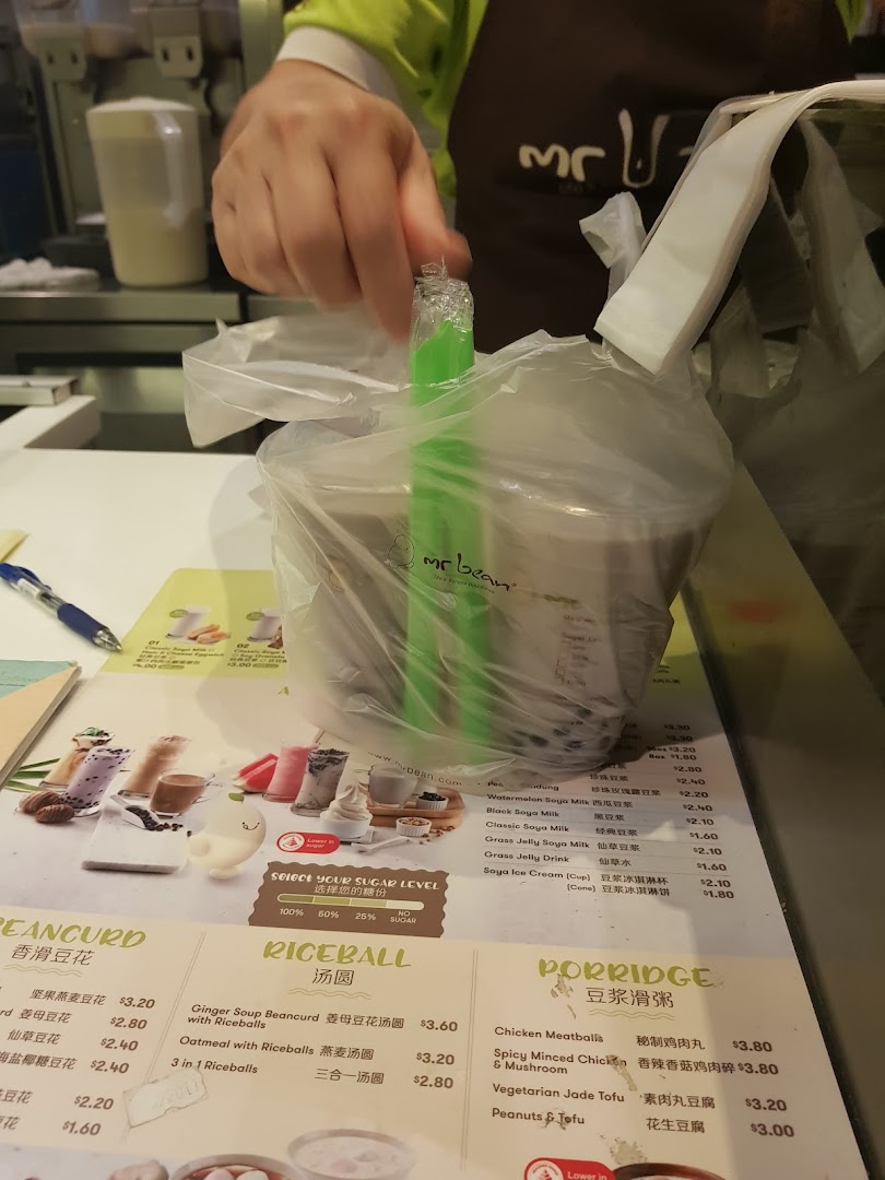 A hand holds a bagged order over a detailed menu at Mr Bean.