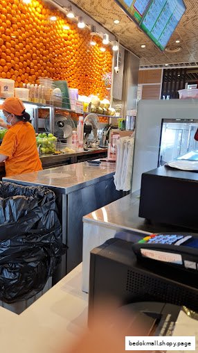 Interior shot of a fruit juice shop with staff and orange display.