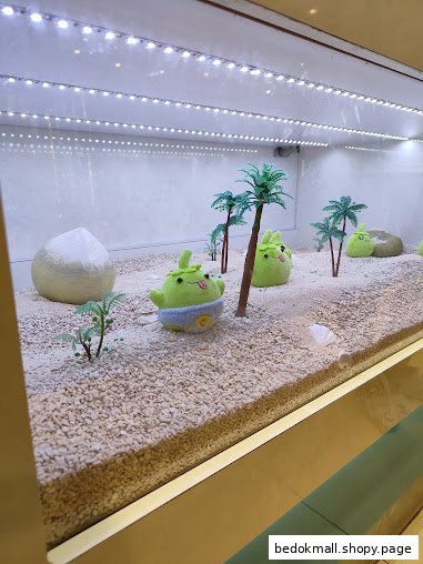 A display case with sand, miniature palm trees, and green plush characters.