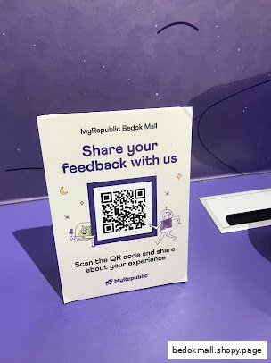 A feedback sign with a QR code on a purple surface.