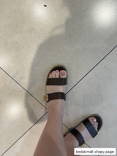 Feet in sandals with painted toenails on a tiled floor.